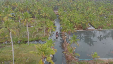 Aerial-view-of-longboats-floating-on-narrow-canals-and-waterways-amidst-palm-trees-of-Munroe-island,-India