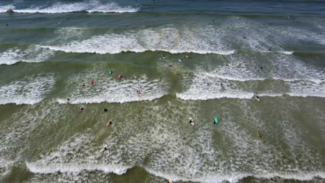 Ojo-De-Pájaro,-Tiro-Con-Dron-De-La-Playa-De-Muizenberg,-Ciudad-Del-Cabo---El-Dron-Desciende-Sobre-Los-Surfistas-Que-Intentan-Atrapar-Una-Ola