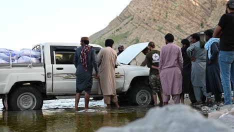 Zwei-Personen-Reparieren-Den-Jeep,-Der-Getreide-Und-Vorräte-Für-Die-Flutopfer-Transportiert,-Und-Andere-Umzingeln-Den-Jeep-In-Belutschistan