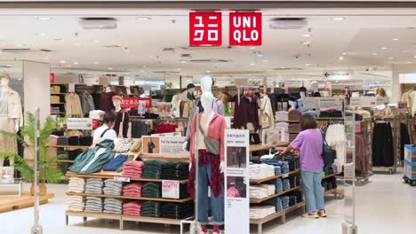 Female-shoppers,-women,-source-and-buy-fashion-clothes-at-the-Japanese-clothing-brand-Uniqlo-logo-and-store-in-Hong-Kong