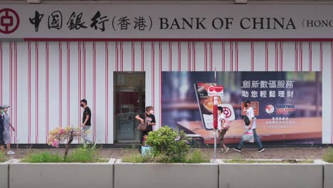 Chinesische-Fußgänger-Gehen-An-Dem-In-Hongkong-Ansässigen-Bank--Und-Finanzdienstleistungsunternehmen-Und-Dem-Hauptindikator-Für-Den-Hongkonger-Aktienmarkt,-Der-Hang-Seng-Bank-Und-Einer-Filiale-In-Hongkong-Vorbei