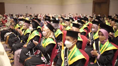 Happy-graduates-in-hats-and-robes-siting-in-row-and-applauding