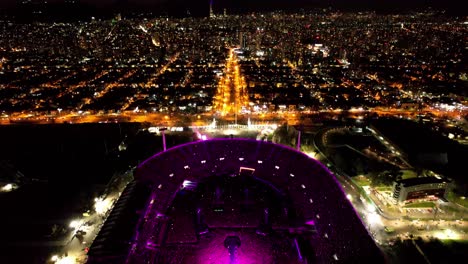 Vista-Aérea-De-Un-Gran-Concierto-Nocturno-Con-Luces-Moradas-En-La-Noche-Con-Miles-De-Fans-En-La-Ciudad-De-Santiago,-Chile