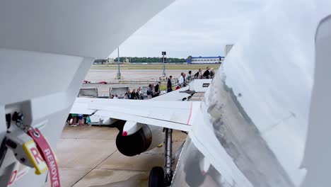 View-from-back-disarmed-opened-door-of-passengers-embarking-from-stairs-with-aircrafts-parked-at-London-Gatwick-airport,-UK
