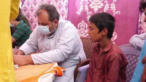 Un-Médico-Con-Mascarilla-Y-Hablando-Con-El-Niño-Sobre-Su-Dolencia-En-El-Campamento-De-Ayuda-Contra-Inundaciones-Instalado-En-Sindh,-Pakistán