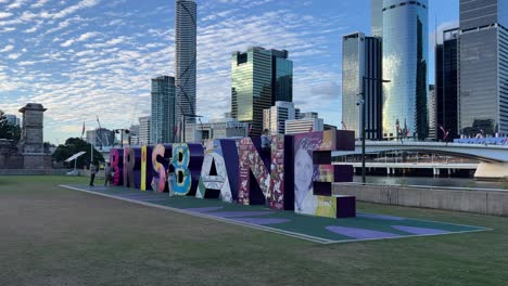 Children-happily-dancing-in-front-of-the-iconic-landmark-block-sign-of-Brisbane-on-a-beautiful-afternoon-with-downtown-cityscape-and-victoria-bridge-as-backdrop,-Queensland,-Australia