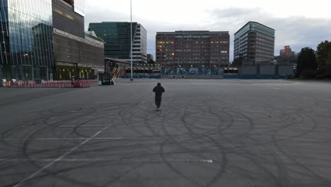 Chasing-a-young-man-while-he-rides-an-electric-rental-scooter-and-vapes-in-an-empty-lot,-aerial