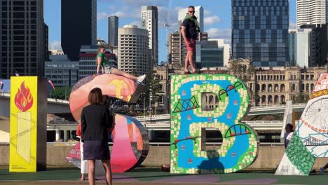 People-having-fun-climbing-up-and-down-the-artistic-block-letter-and-taking-photos-with-the-iconic-landmark-of-Brisbane-City-on-a-sunny-day,-Queensland,-Australia,-close-up-handheld-motion-shot