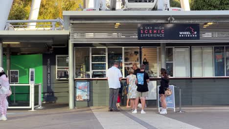 People-lining-up-at-ticket-counter-to-go-on-gondola-ride-on-channel-seven-wheel-of-Brisbane,-iconic-landmark-ferris-wheel-scenic-experience-at-South-bank-parklands,-Queensland,-Australia