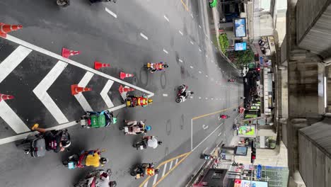 Vertical-video---A-Top-view-of-motorcyclists-waiting-at-the-traffic-lights-intersection-in-Bangkok,-Thailand