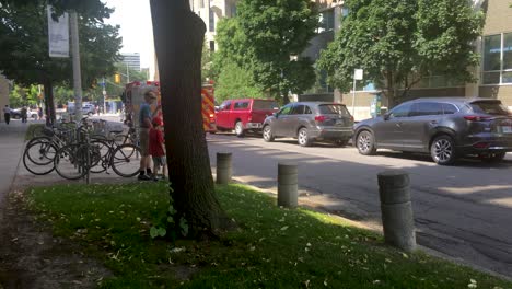 Toma-Panorámica-Constante-De-Un-Cuerpo-De-Bomberos-Que-Se-Precipita-Hacia-El-Lugar-De-Un-Accidente-Con-Las-Luces-De-Alarma-Parpadeando,-En-Una-Carretera-Con-Automóviles-Estacionados-A-Ambos-Lados