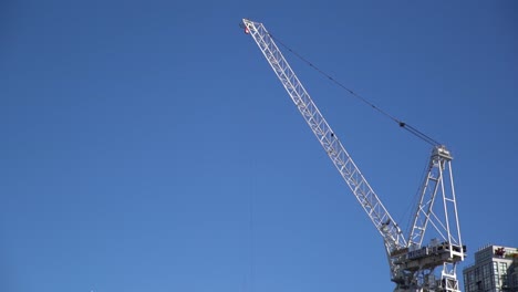 White-construction-crane-stands-tall-above-city-skyline-against-blue-skies