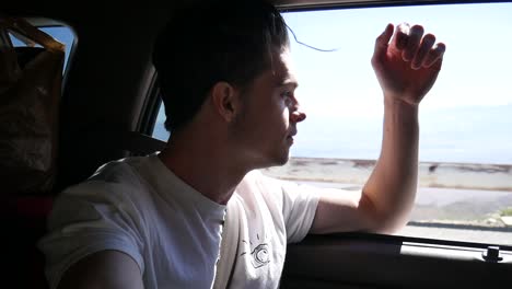 Joven-Hombre-Feliz-En-Coche-Mirando-Por-La-Ventana-Con-El-Paisaje-De-Fondo