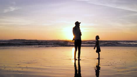 Eine-Mutter-Genießt-Mit-Ihren-Beiden-Kindern-Den-Sonnenuntergang-Am-Strand,-Während-Ihre-Tochter-Auf-Sie-Zuläuft-Und-Fragt,-Ob-Sie-Spielen-Dürfen