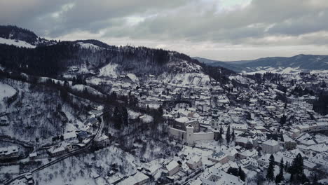 Wide-aerial-shot-of-a-Mining-town-Banska-Stiavnica-in-winter-covered-by-snow,-twilight