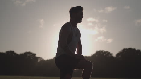 Man-Stretching-His-Legs-Before-a-Run-Whilst-Being-Silhouetted-By-The-Evening-Sun---Ungraded