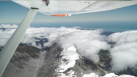 Aerial-shot-from-plane-scenic-flight-over-west-coast-Franz-Josef,-Aoraki-Mount-Cook,-National-Park-with-clouds,-snowcapped-rocky-mountains-and-ocean-in-background