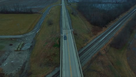 A-car-travels-on-an-overpass-over-railroad-tracks-near-a-lake-in-rural-Southern-Illinois-with-some-light-snow-on-the-ground