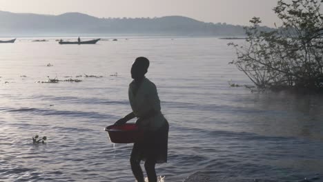 Silueta-De-Una-Mujer-Africana-Recogiendo-Agua-En-Un-Balde-A-Orillas-Del-Lago-Victoria-En-El-Sol-De-La-Madrugada