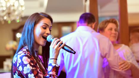 Attractive-girl-singing-at-party-with-a-couple-dancing-to-the-music