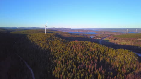 Aerial-rising,-drone-view-towards-forest,-hills,-lakes-and-a-wind-power-generator-turbine,-on-the-top-of-a-mountain,-in-Hoga-kusten,-Sweden