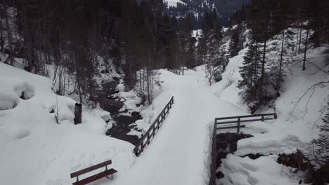 Aerial-view-of-a-small-bridge-over-a-creek-in-a-snowy-valley-in-the-alps,-Kleinwalsertal,-Austria