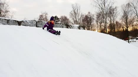 Mädchen,-Das-Draußen-Spielt-Und-Bei-Klarem-Winterwetter-Einen-Verschneiten-Eishügel-Auf-Dem-Hintern-Hinunterrutscht