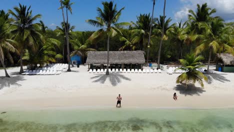 Aerial-orbit-shot-of-a-man-standing-on-the-shore-piloting-the-drone,-an-island-in-Carribean