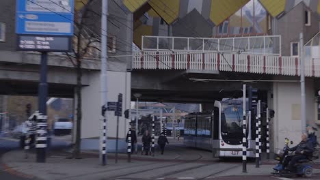 Close-up-of-a-tram-passing-by-continuing-underneath-the-overhead-famous-architecture-of-the-overhanging-cube-houses-in-the-city-centre-of-Rotterdam,-The-Netherlands