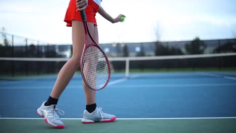 A-woman-bouncing-a-ball-and-jumping-to-warm-up-before-she-begins-her-tennis-match