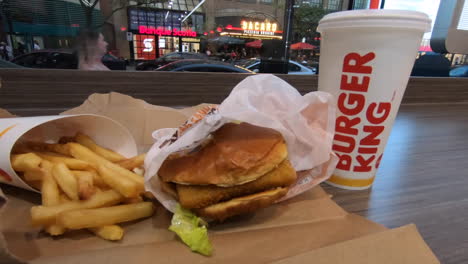 Editorial,-View-of-Burger-King-hamburger,-sandwich,-fries-and-fresh-drink,-coca-cola,-meal-on-counter-beside-the-window-street-view-of-people-passing