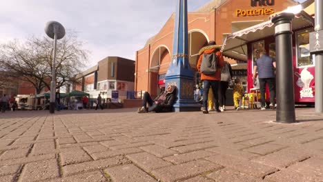 A-homeless-man-asleep-in-the-city-centre-people-just-walking-by-outside-the-biggest-shopping-centre-in-the-city,-Intu-Potteries,-Time-lapse