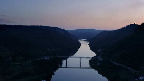 Schöne-Brückenreflexion-Auf-Dem-Fluss,-Zwischen-Silhouettenbergen
