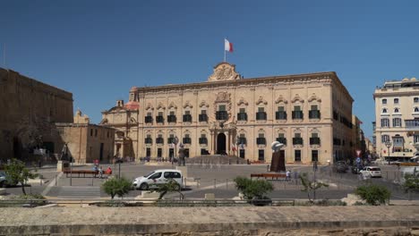 Timelapse-of-the-busy-Auberge-De-Castille,-Valletta-after-restoration,-with-a-Maltese-flag-flattering-on-top-of-the-buildin