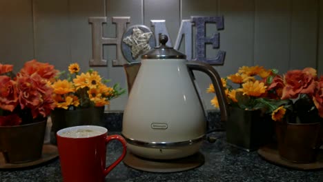 Hand-takes-steaming-cup-of-coffee-from-kitchen-counter-next-to-retro-electric-kettle,-static