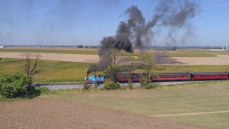 Aerial-View-of-Thomas-the-Train-Puffing-Black-Smoke-and-Pulling-Passenger-Cars-full-of-Happy-Children-on-a-Sunny-Day-as-Seen-by-a-Drone