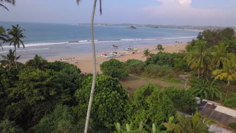 Aerial-dolly-tilt-of-beach-in-Weligama,-Sri-Lanka-with-fishing-boats-in-the-background