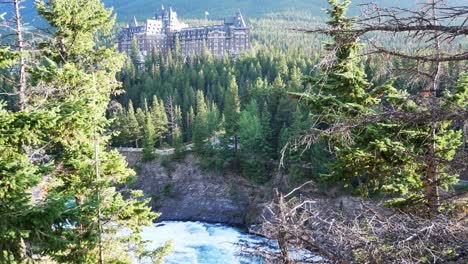 Fairmont-Banff-Springs-in-Banff-Town,-Alberta,-Canada-together-with-bow-river-fall-in-sunset-time-among-the-pine-tree-forest-with-clear-blue-sky-and