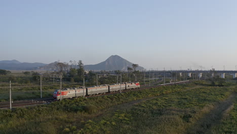 Locomotoras-De-Trenes-Rusos-Se-Mueven-A-Través-De-Los-Campos-Con-Montañas-En-El-Fondo-De-La-Puesta-Del-Sol,-Federación-Rusa