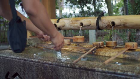Person-washing-his-hands-early-morning-the-traditional-way,-water-pouring-out-of-bamboo-in-Kyoto,-Japan-soft-lighting-slow-motion-4K
