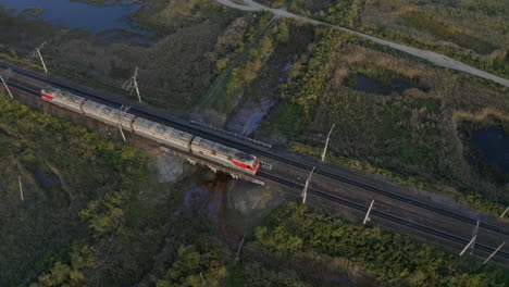 Vista-Superior-De-Las-Locomotoras-Del-Tren-Ferroviario-Ruso-Se-Mueven-A-Través-De-Campos-Verdes,-Al-Atardecer,-Federación-Rusa