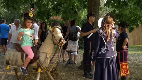 Carnaval-Savaria,-Niño-Hussar-Enseñando-A-Una-Niña-A-Montar-Un-Caballo-De-Madera-Hablando-Con-Un-Civil