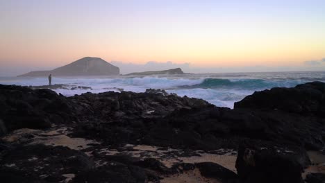 High-tide-rushing-over-the-tide-pools-of-Makapuu-Beach-at-sunrise-with-a-photographer-holding-a-camera-in-the-far-distance