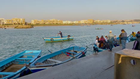 Families,-tourists-and-lovers-taking-boat-rides-across-the-Bou-Regreg-inlet-in-Rabat,-Morocco-by-the-Avenue-Al-Marsa-at-sunset---time-lapse
