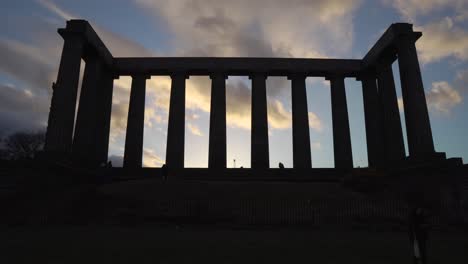 Statische-Silhouettenaufnahme-Des-Nationaldenkmals-Von-Schottland-Und-Silhouetten-Von-Menschen-Mit-Einem-Wunderbaren-Sonnenuntergangslicht-Und-Wolken-Vom-Calton-Hill-In-Edinburgh,-Schottland
