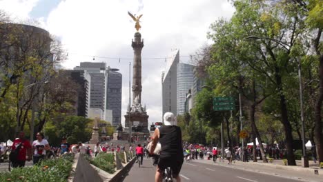 people-cycling-on-avenue-paseo-de-la-reforma,-during-a-sunny-sunday-with-the-independence-angel-on-the-back-ground