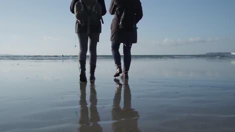 Two-women-walking-on-a-wet-beach-on-a-cold-and-sunny-day