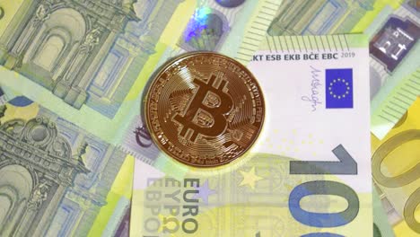 Spinning-Shot-Of-Shining-Golden-Bitcoin-Laying-On-Top-Of-Layer-of-Hunded-Euro-Banknotes
