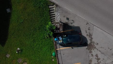 Woman-tracing-a-route-on-a-map-of-the-Dolomite-mountains-in-Northern-Italy-on-top-of-her-car-hood-while-parked-in-a-small-village-town,-Drone-top-view-with-lift-shot