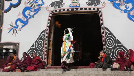 Traditional-Buddhist-Tibetan-Cham-dancing-ceremony-on-monastery-steps-as-monks-sitting-watching